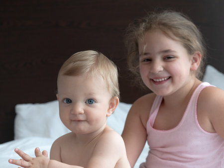 Two cute little sisters sitting on the bed and smiling at camera.の写真素材