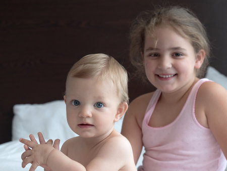 Cute little girl and her sister playing on the bed at homeの写真素材