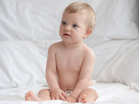 Cute baby boy sitting on bed and looking at camera over white backgroundの写真素材
