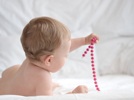 Cute little baby playing with beads on white bed, closeupの写真素材