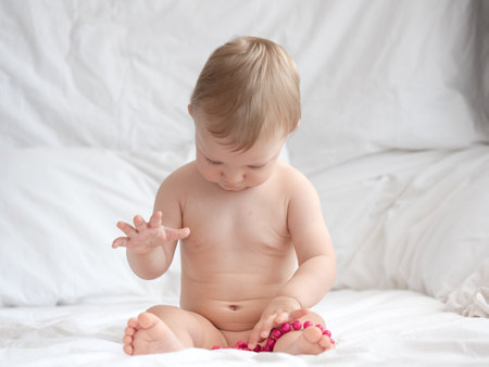 Cute baby girl playing with beads on the bed at home.の写真素材