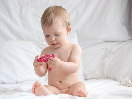 Cute little baby girl playing with red beads on white bed.の写真素材