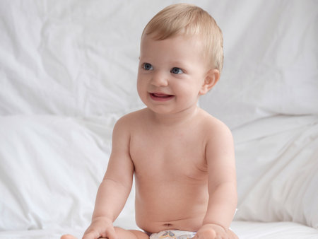 Cute baby sitting on white bed and looking at camera.の写真素材