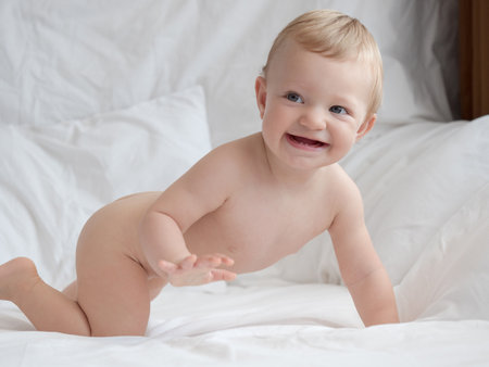 Portrait of cute smiling baby boy on bed at home. Adorable child having fun on the bedの写真素材