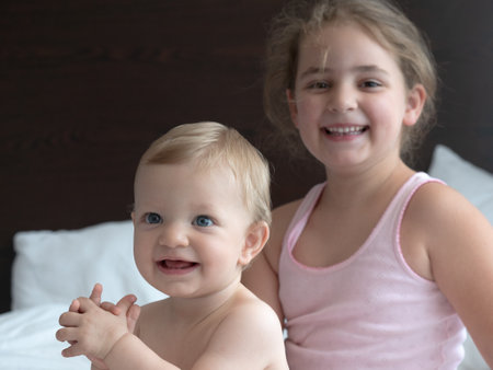 Portrait of a smiling little girl and her sister on the bedの写真素材