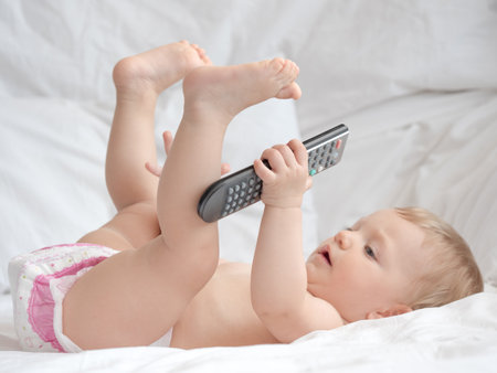 Cute little baby with remote control on bed at home, closeupの写真素材