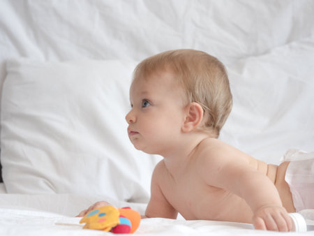 Cute baby lying on bed and playing with toy on white backgroundの写真素材