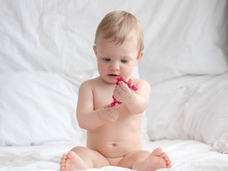 Cute little baby playing with raspberries on bed at homeの写真素材