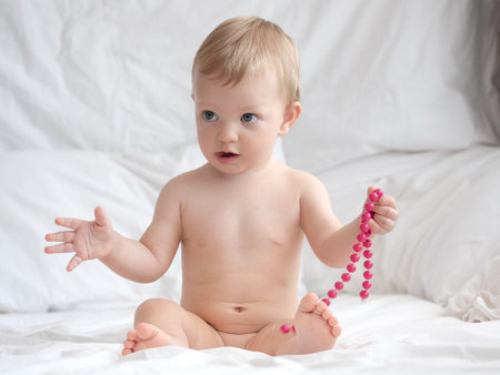 Cute baby boy playing with beads on the bed at home.の写真素材