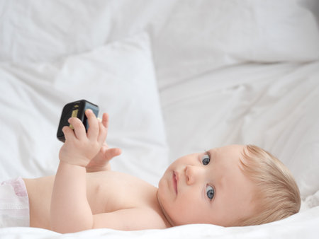 Cute little baby playing with mobile phone on bed, closeupの写真素材
