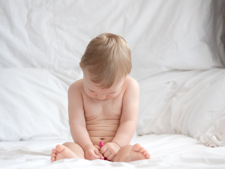 Cute baby boy sitting on bed and playing with toy on white backgroundの写真素材
