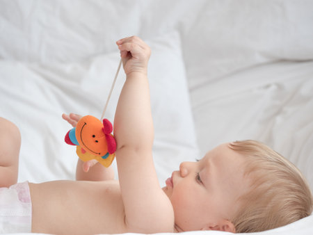 Cute little baby playing with toy on bed at home, closeupの写真素材