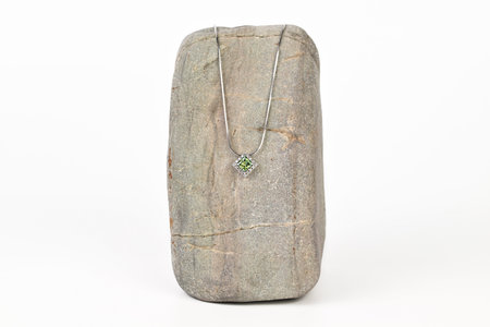 A necklace is displayed on a rock. The necklace is silver and has a green stone. The rock is grey and has a rough texture. The necklace and rock together create a sense of natural beautyの写真素材