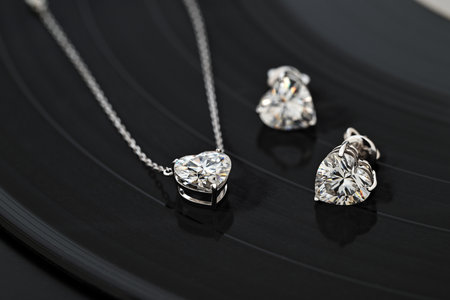 A necklace and earrings set made of diamonds are displayed on a black record. The earrings are shaped like hearts and the necklace is a pendantの写真素材