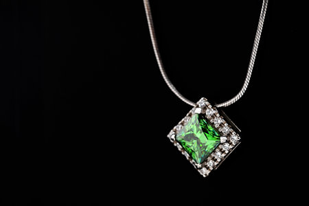A green gemstone pendant is displayed on a black background. The pendant is made of silver and has a...