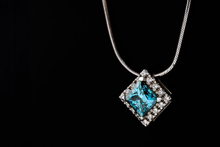 A blue and white necklace sits on a black surface. The necklace is made of silver and has a diamond...