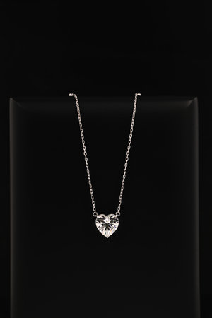 A heart shaped pendant with a chain is displayed in a black box. The pendant is made of clear glass and is set with diamonds.の写真素材