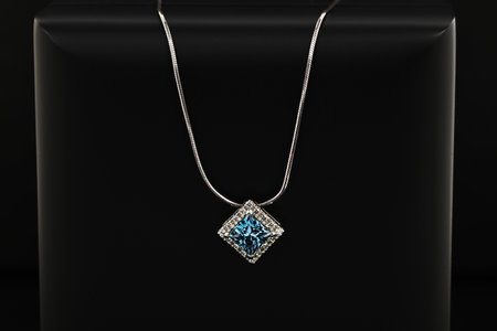 A blue and white necklace on a black surface. The necklace is made of silver and has a diamond pendant. The necklace is simple and elegant, with a modern designの写真素材