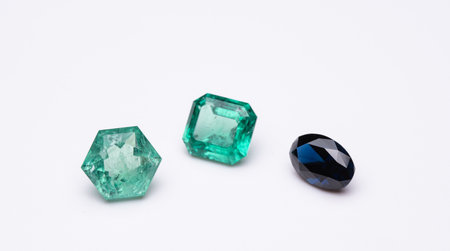Three different colored gemstones are displayed on a white background. The green gemstone is the largest and is surrounded by two smaller stonesの写真素材