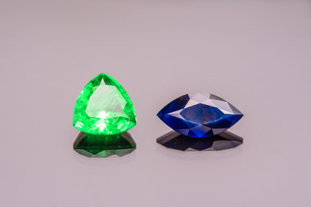 Two gemstones, one green and one blue, are displayed on a table. The green stone is a triangular shape, while the blue stone is a round shape. The stones are placed next to each otherの写真素材