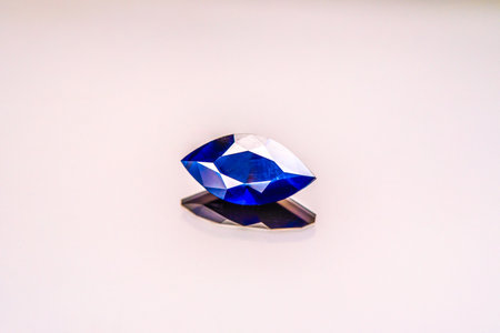 A blue gemstone is sitting on a white surface. The stone is cut into a diamond shape and is reflecting lightの写真素材