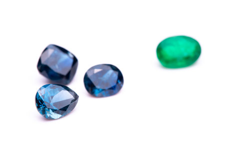 A collection of gemstones, including a green emerald, are displayed on a white background. The...