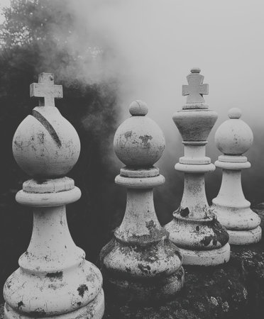 Four white chess pieces are sitting on a stone surface. The pieces are all different sizes and are...