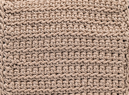 A tan and white knitted item with a pattern of knots. The item is made of yarn and has a fuzzy...