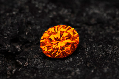 A large orange diamond is sitting on a black rock. The diamond is the center of attention and the...