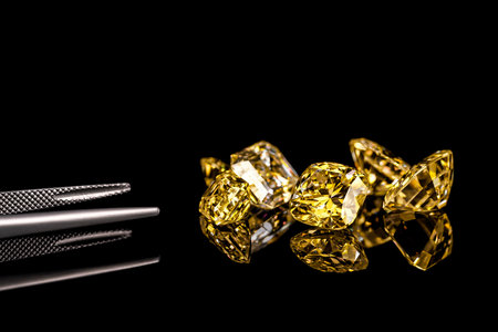 A close up of yellow diamonds with a pair of tweezers on the left. The diamonds are arranged in a row.の写真素材