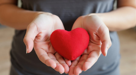 A woman is holding a red heart in her hands. The heart is soft and fuzzy, and it is a gift. The woman's hands are open and welcoming, suggesting that the heart is meant to be given to someone specialの写真素材