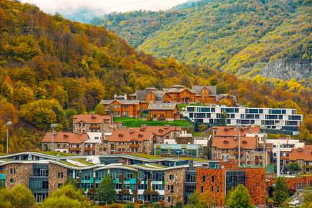 A small town with houses and a church. The houses are mostly brown and white. The town is surrounded by trees and mountainsの写真素材