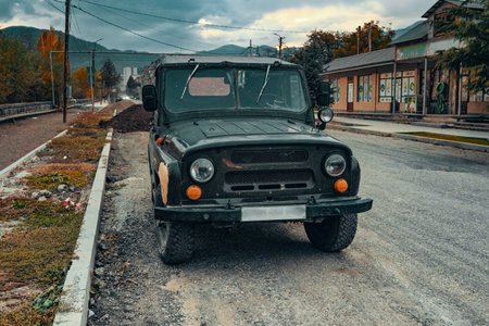 A black vintage jeep is parked on the side of a road. The jeep is dirty and has a few scratches on it. The road is empty and there are no other vehicles in sight. The scene gives off a sense of lonelinessの写真素材