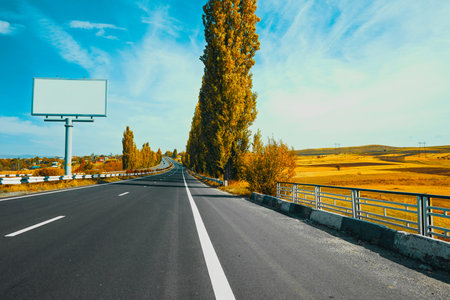 A highway with a large billboard in the background. The billboard is white and the sky is blueの写真素材