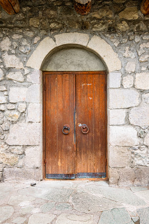 Old wooden door with a stone archway. The door is old and rusted. The stone wall behind the door is greyの写真素材