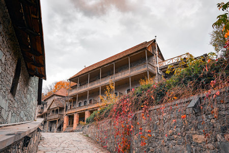 An old stone building with a red roof and a stone wall. The building has a balcony and a staircase