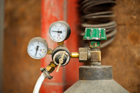 A pressure gauge is attached to a cylinder container. The gauge is green and white. The container is redの写真素材