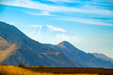 A mountain range with a snow covered peak in the distance. The sky is clear and blue.