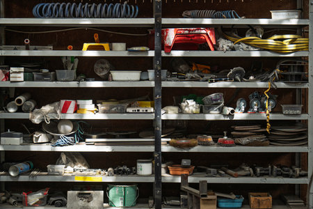 A disorganized shelf with many items on it. The items are scattered and disorganized, with some items being piled on top of each other. The shelf appears to be in a workshop or garageの写真素材