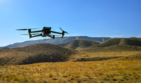 A drone is flying over a desert landscape. The drone is black and white and is flying low to the...