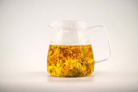 A glass of Chamomile tea with flowers floating in it. The tea is yellow and the flowers are whiteの写真素材