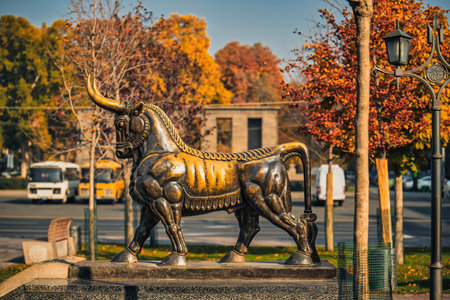 Yerevan Armenia 11.20.2025. A statue of a bull with a golden mane and horns. The statue is surrounded by trees and parked carsのeditorial素材