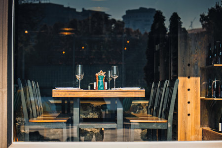 Yerevan Armenia 11.20.2025. A restaurant table with a large number of chairs and a glass of wine. The table is set with wine glasses, a bottle, and a bowl. Scene is that of a formal dinner settingの写真素材