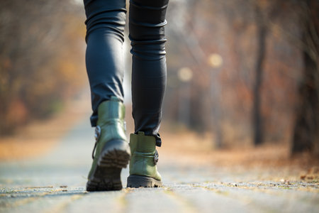A woman is walking on a path in the woods. She is wearing green boots and black pantsの写真素材