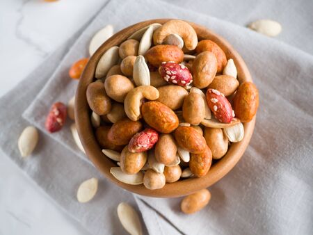 Crispy assorted mixed nuts with different flavors and pumpkin seeds in the wooden bowl and grey linen towel as background. Roasted nuts coated by salt and spicy. Snack for beer. Close up. Top view.の写真素材