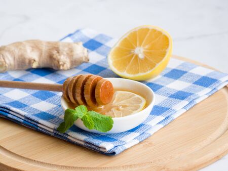 Organic natural ingredients concep. Products for health and immunity. Honey in white bowl with honey dipper or stick, lemon, ginger and mint in blue and white linen towel as background.の写真素材