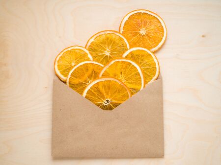 Healthy snack. Closeup Healthy mood. Eco organic homemade dried orange slices, chips, in a craft envelope on wooden background . Dehydrated crispy fruit slices. Heap, pile of sun dried crunchy oranges.の写真素材