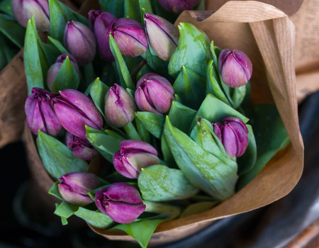 Bunches of purple tulip wrapped in craft paper for sale. Fresh spring lilac flowers. Colorful...
