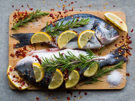Fresh uncooked dorado or sea bream fish with lemon slices, spices, herbs and rosemary on cutting board. Mediterranean cuisine. Top viewの写真素材