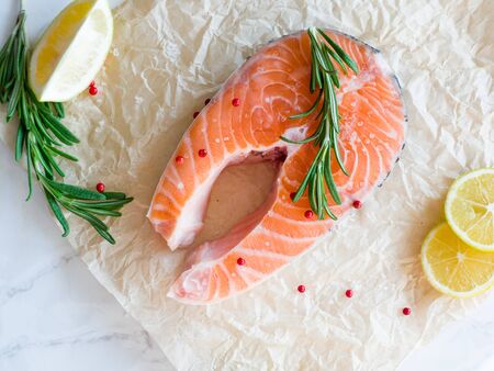 Delicious salmon steak with lemon slices, spices and rosemary , rich in omega 3 oil, on light table. Healthy and diet food. Fresh uncooked red fish. Cooking salmon, seafood. Top viewの写真素材